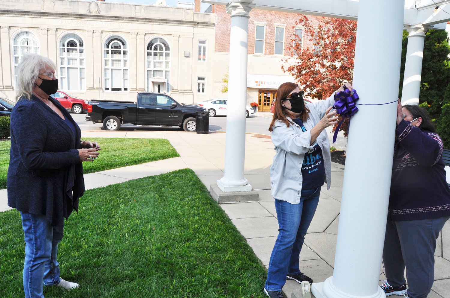 Joyce Baker, left, watches Deb Lee and Kathy Walker tie a purple ribbon representing domestic violence awareness at Marie Canine Plaza Tuesday. October is Domestic Violence Awareness Month.